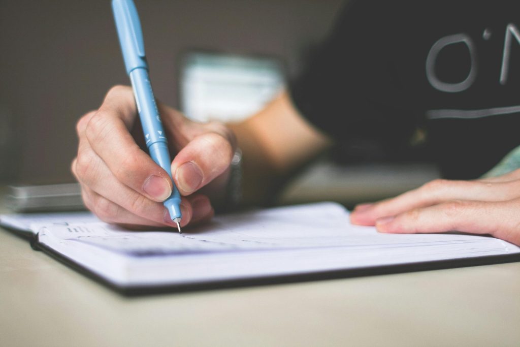 Primer plano de una mano escribiendo en un cuaderno con un bolÃgrafo azul, concentrándose en la creatividad.