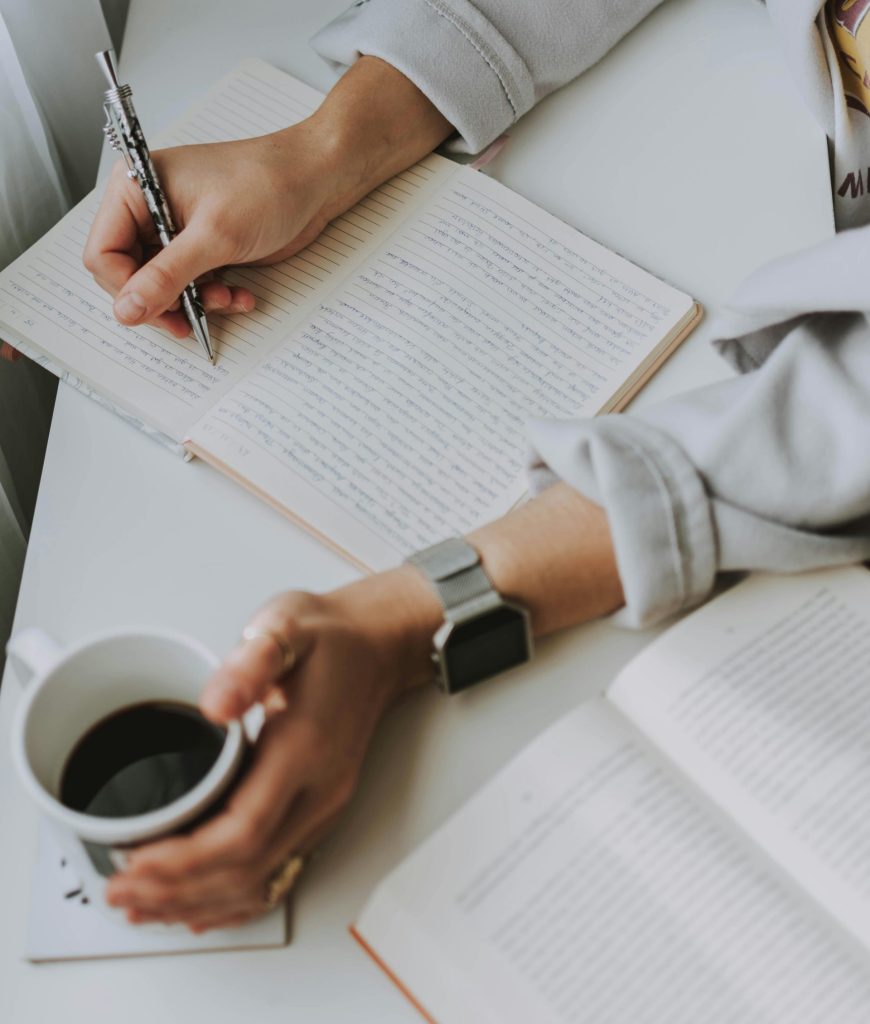 Primer plano de una persona escribiendo en un cuaderno con café sobre un escritorio. Ideal para el trabajo o el estudio.