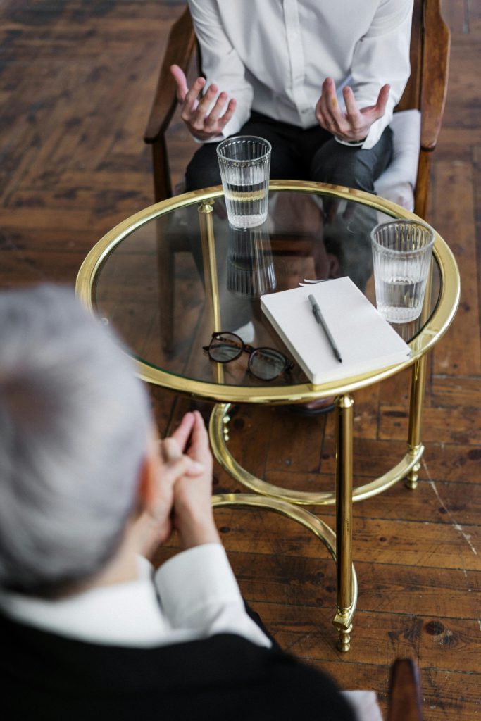 Dos adultos discuten sobre salud mental en una sesión de asesoramiento frente a una mesa de vidrio en el interior.