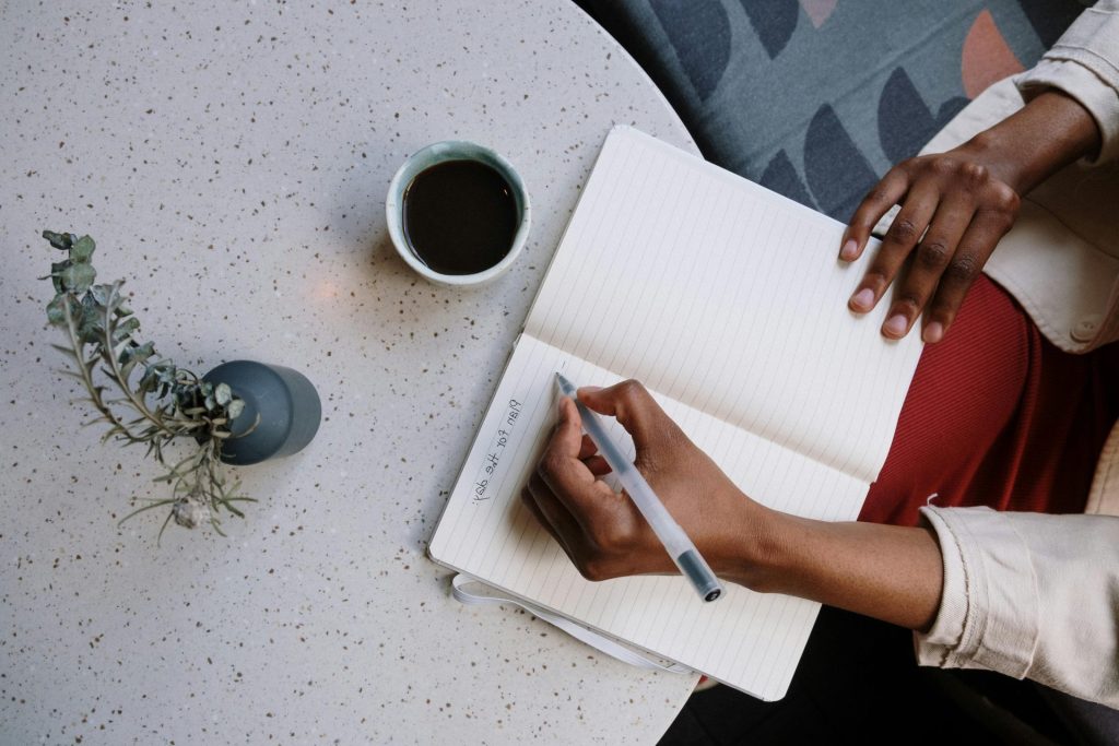 Persona escribiendo en una agenda con café en una cafeterÃa, centrándose en la planificación y la productividad.