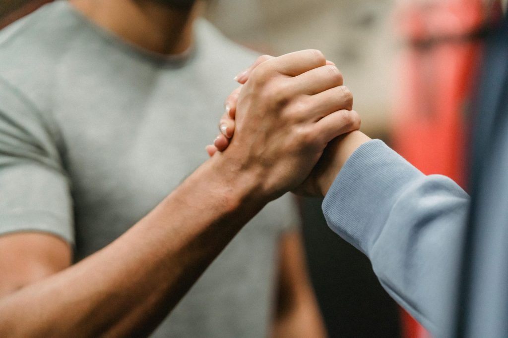 Primer plano de un apretón de manos entre dos personas en un gimnasio, que simboliza apoyo y trabajo en equipo.