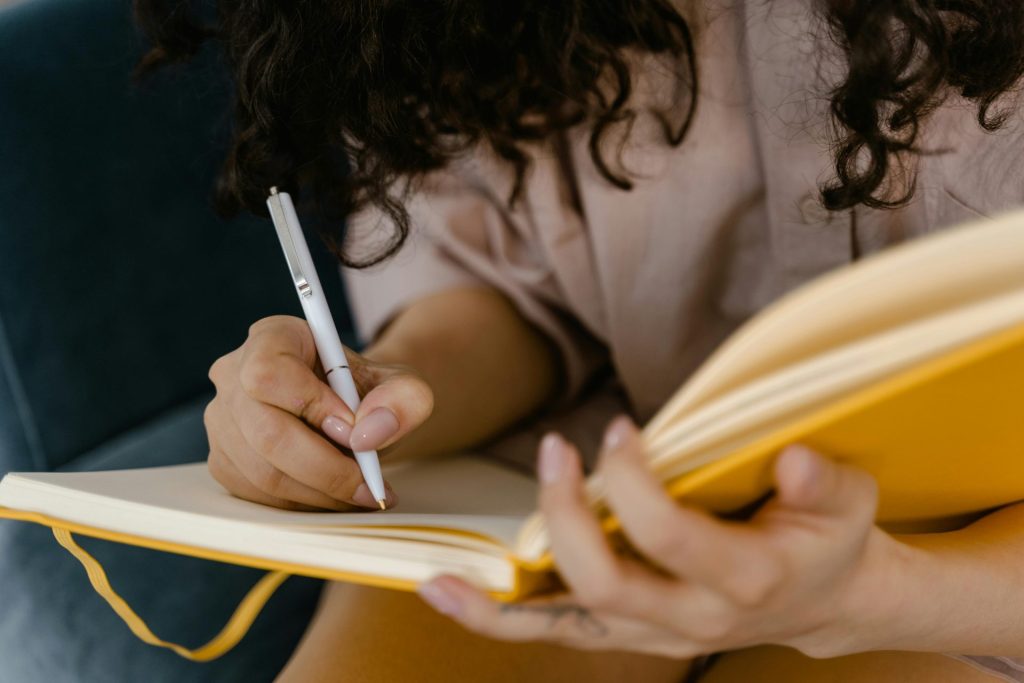 Persona escribiendo en un cuaderno amarillo en el interior, centrándose en las ideas.